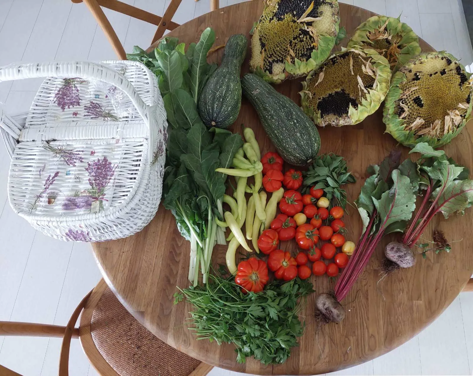 Holztisch mit frisch geerntetem Gemüse: Zucchini, Tomaten, Bohnen, Mangold und Sonnenblumen
