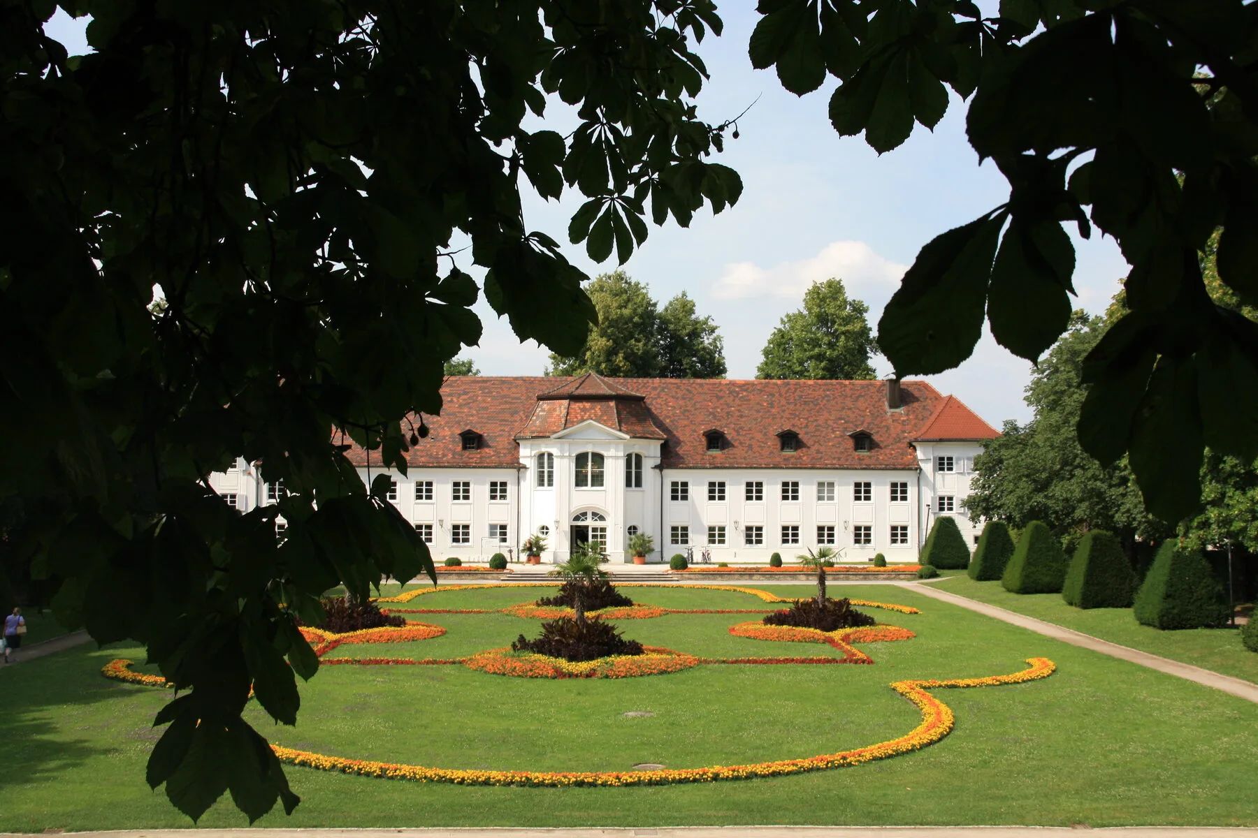 A baroque orangery with a white facade and ornamental garden in summer