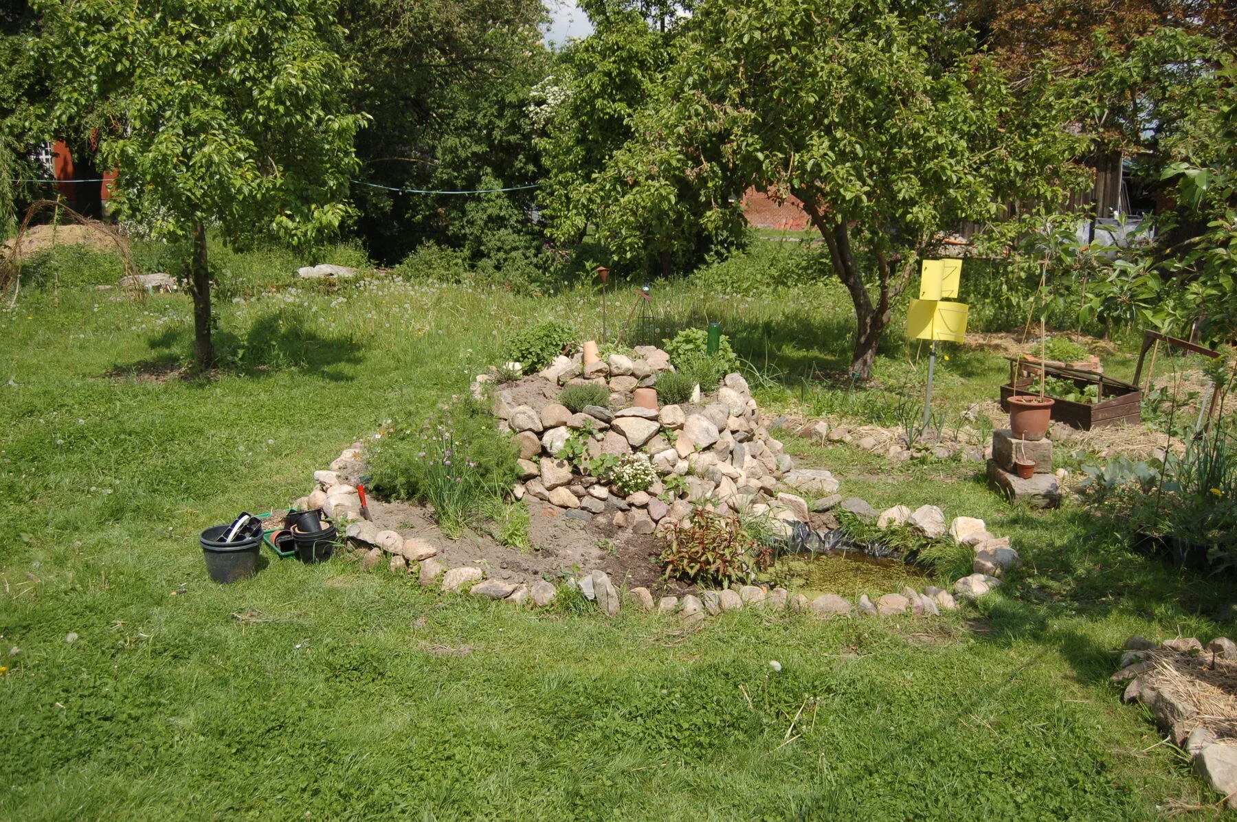 Eine im Bau befindliche Kräuterspirale aus Natursteinen mit kleinem Teich am Fuß
