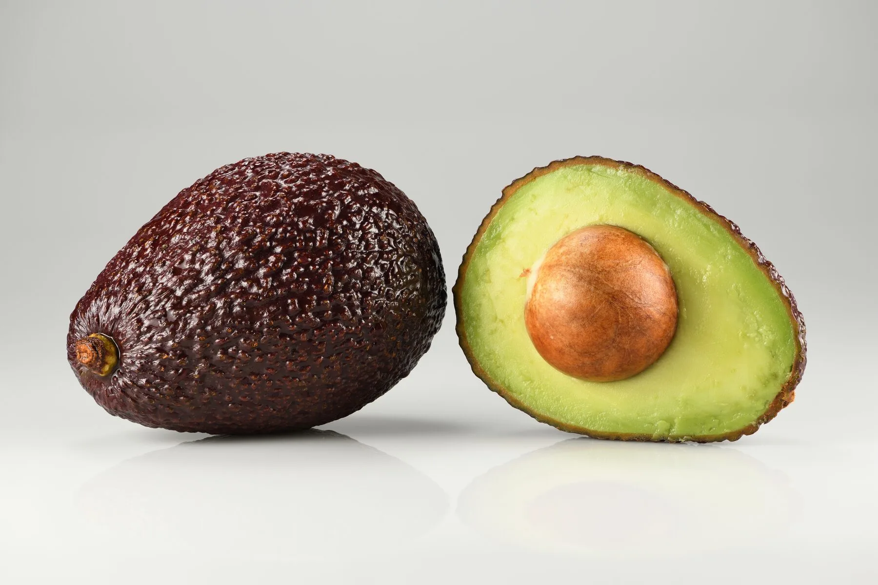 Eine ganze und eine halbierte Avocado der Sorte Hass mit Kern