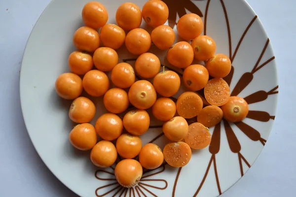 Reife orangegelbe Andenbeere aus ihrer papierartigen Lampionhülle geschält, daneben weitere Früchte in geschlossenen Hüllen