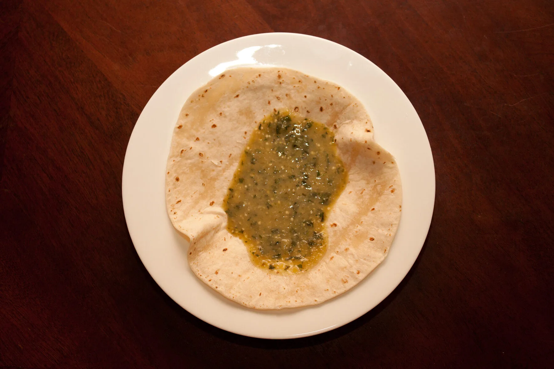 Gruene Salsa Verde auf einer weichen Tortilla auf weissem Teller