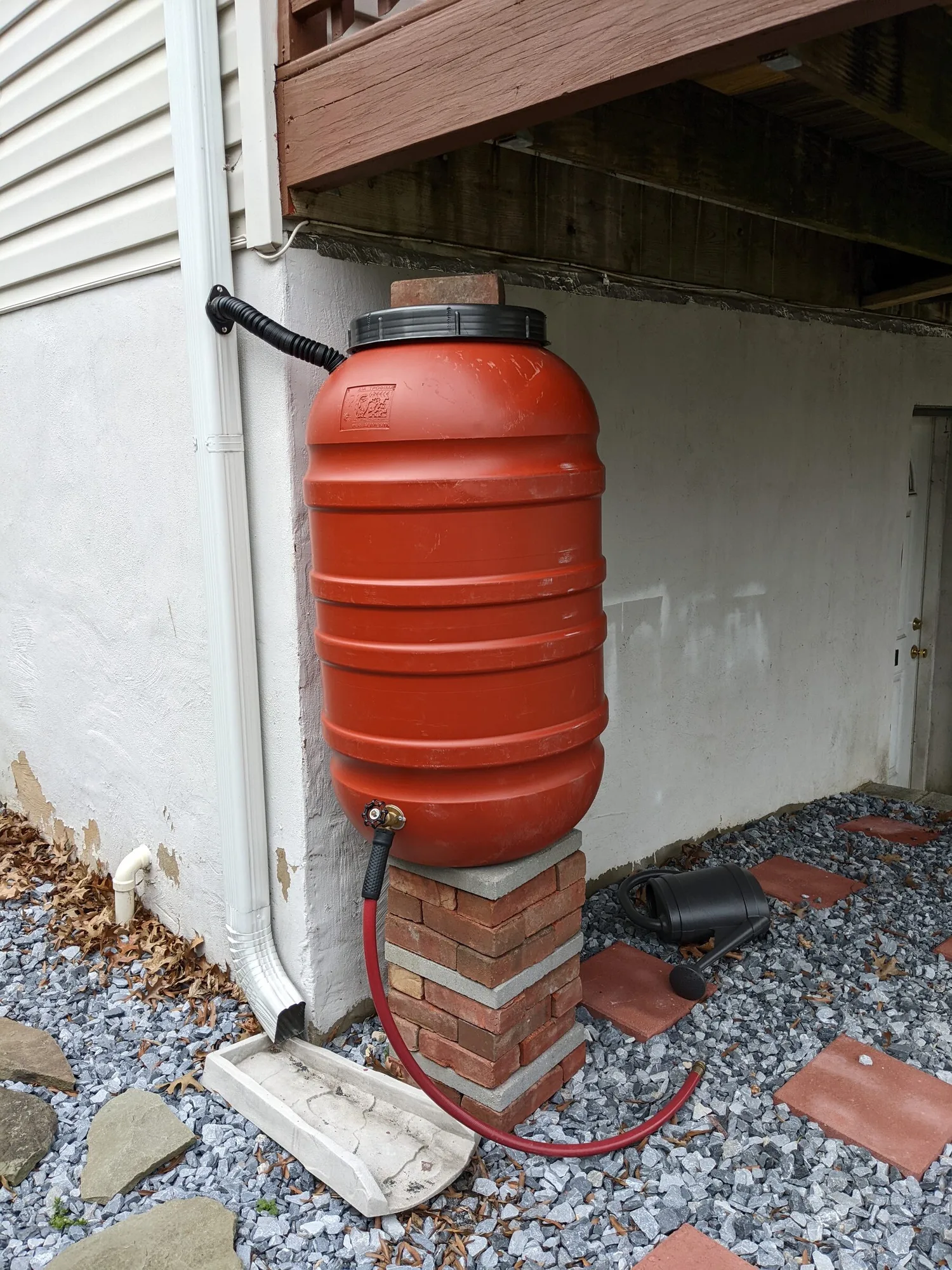 Rote Regentonne am Fallrohr eines Hauses, angeschlossen an die Dachrinne