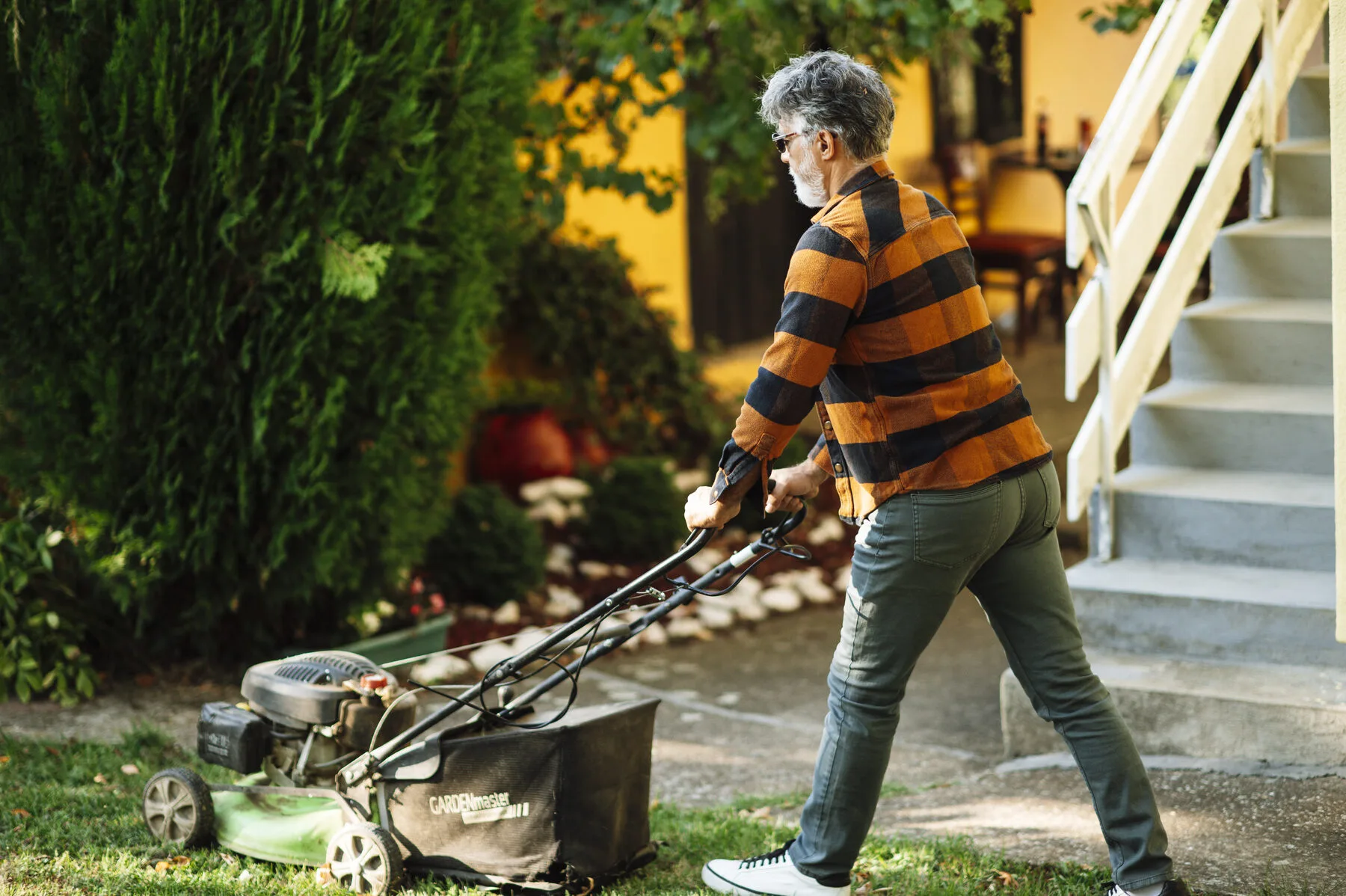 Mann mäht mit einem Handrasenmäher den Rasen in einem Hausgarten