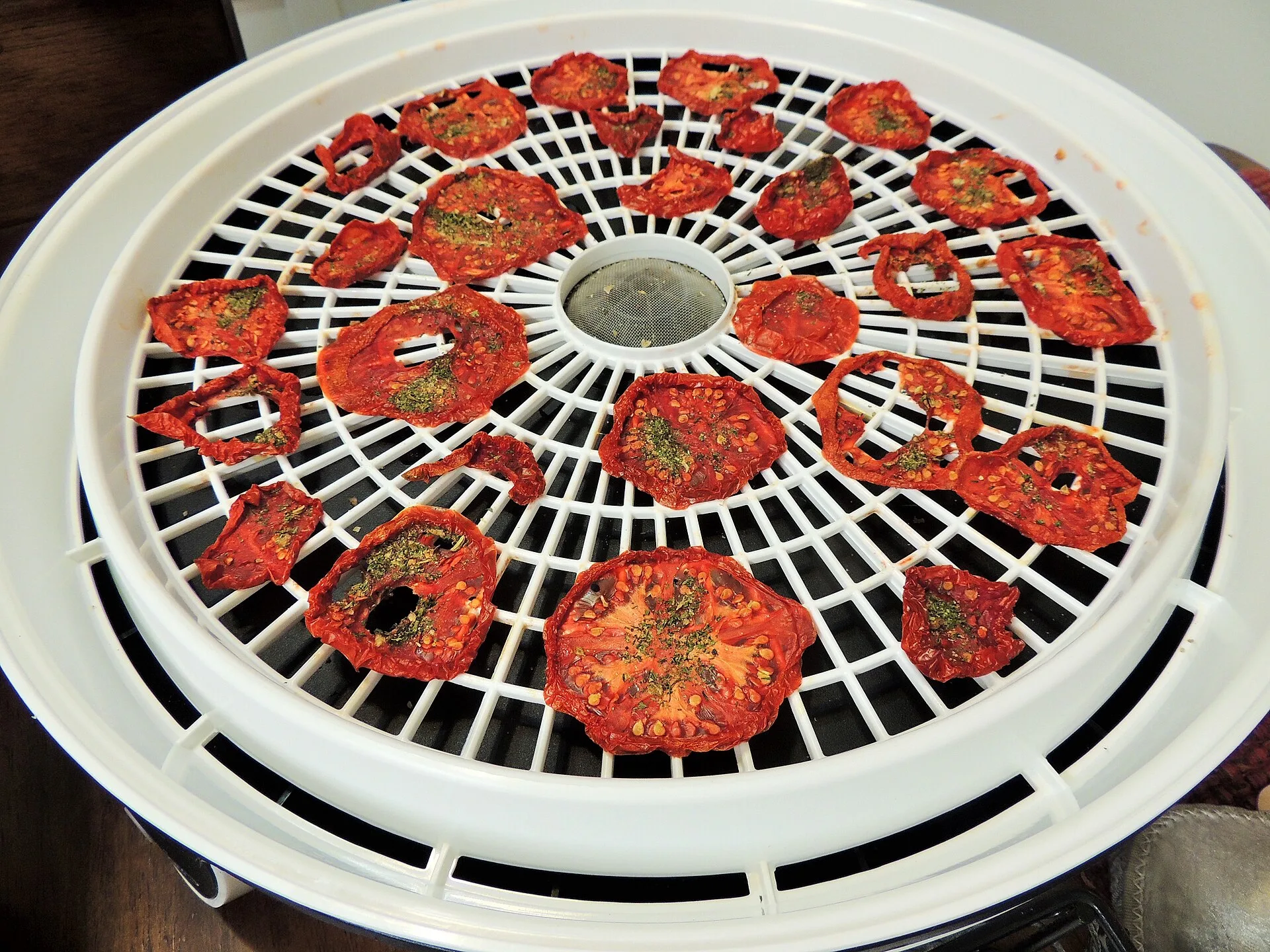 Getrocknete Tomatenscheiben mit aufgestreuten Kräutern liegen auf dem Gitter eines Dörrautomaten