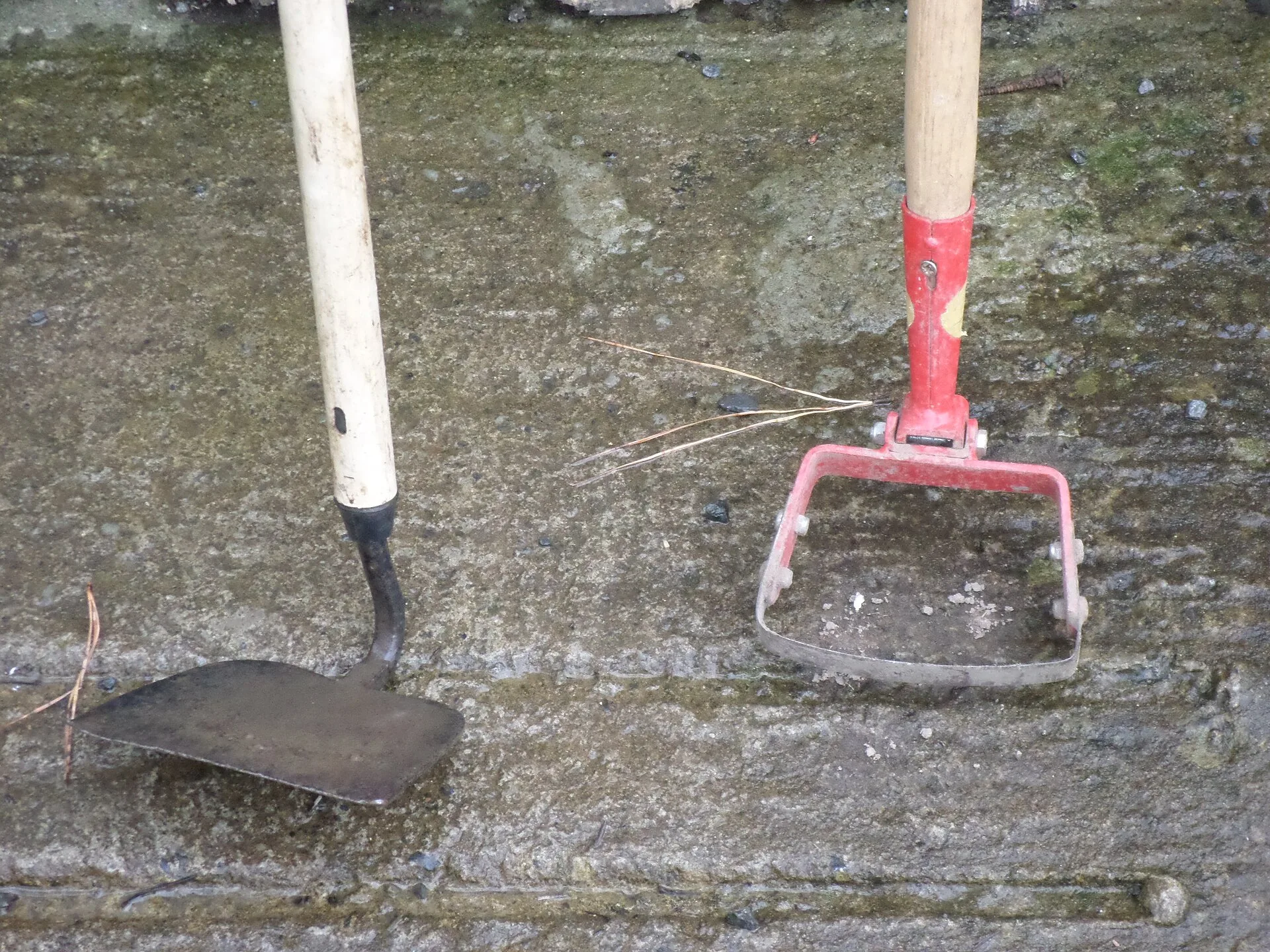 Zwei Hacken nebeneinander auf Beton: links eine Ziehhacke mit starrem rechteckigem Blatt, rechts eine Pendelhacke mit offenem Bügel und beweglicher Schneide
