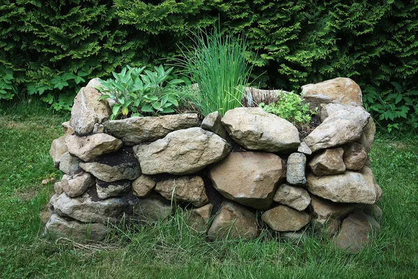 Hochbeet aus aufgeschichteten Natursteinen, oben wachsen Salbei, Schnittlauch und Petersilie